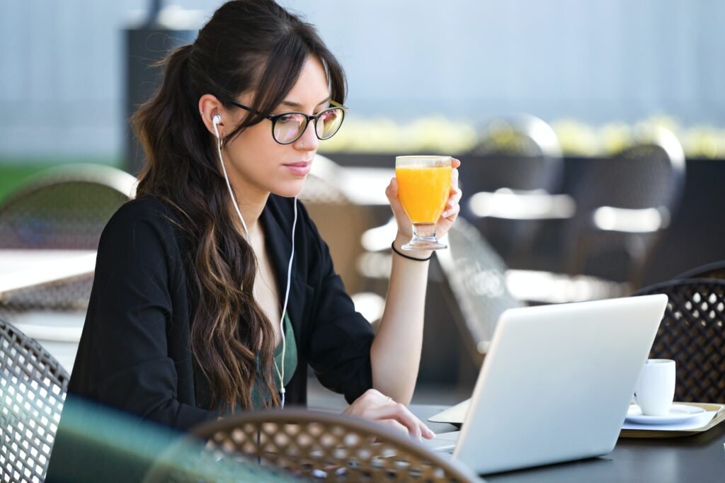 Beautiful young woman drinking orange juice while working with h